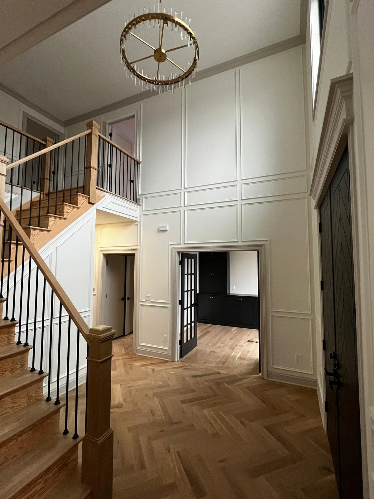 Two-story paneled foyer with a custom staircase and herringbone floors crafted by Lyons Trimming Work LLC